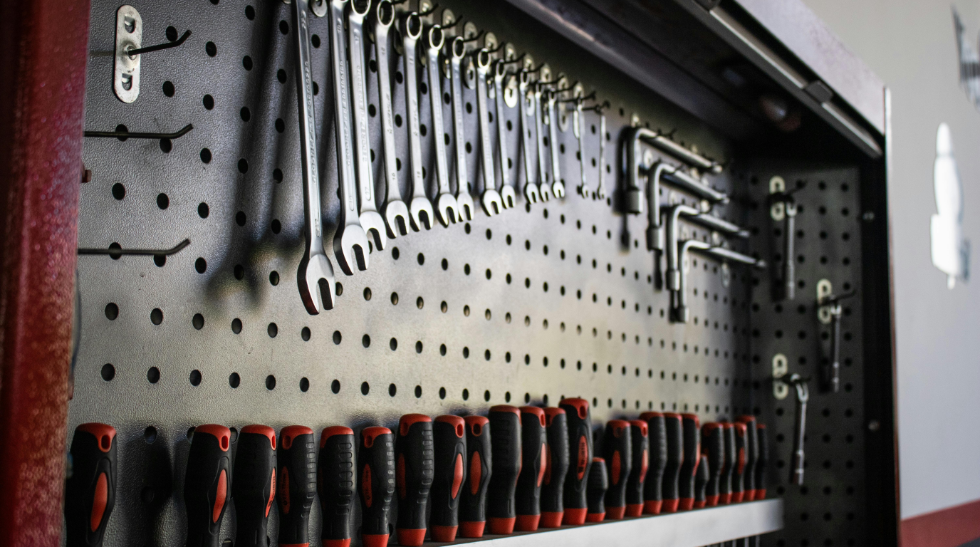 A pegboard wall in a garage hung with hand tools, a level, clamps, and a cordless drill, with everything visible and within reach