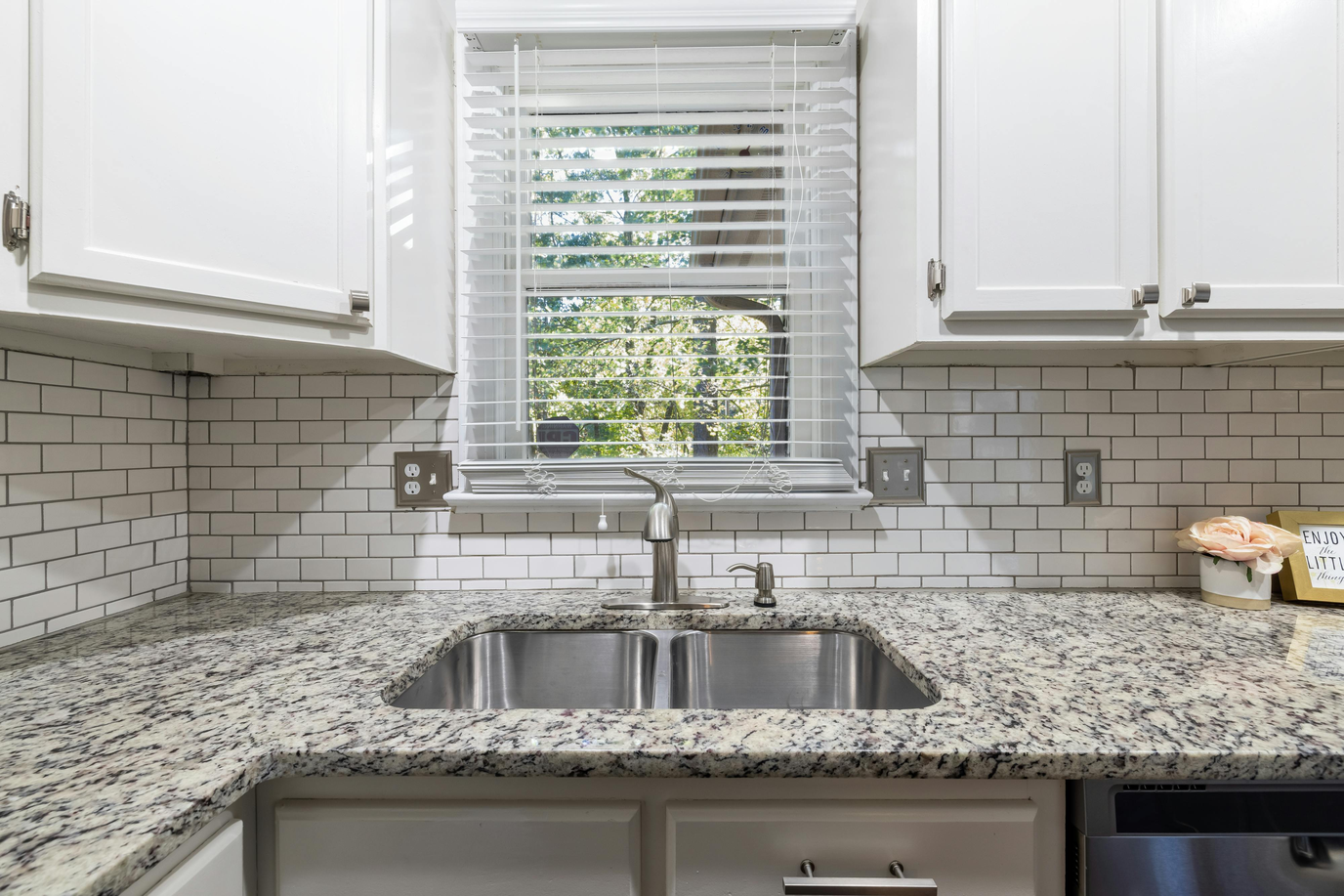 A finished kitchen with a fresh white subway tile backsplash above a granite countertop and a window over the sink