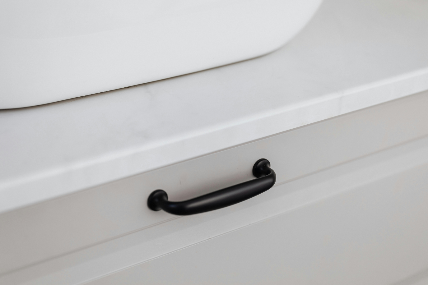 Close-up of a sleek black bar pull on a clean white kitchen drawer front, minimalist modern hardware